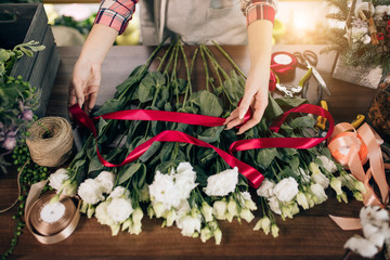 Fototapeta na wymiar top view on florist woman tying bouquet of flowers with red ribbon, florist in her own flowers shop enjoy work with plants, preparing them for sale