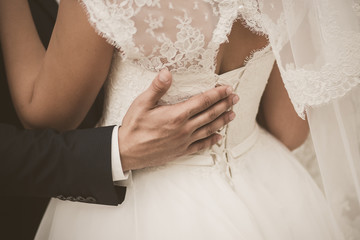 Closeup view photography of back of young bride and male hand of groom hugging waist of woman. Photo filtered in vintage sepia colors.