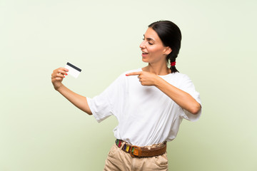 Young woman over isolated green background holding a credit card