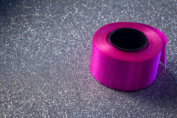 Pink color ribbon roll used in party decorations over glitter background. Party supplies.