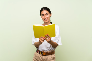 Young woman over isolated green background holding and reading a book
