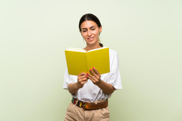 Fototapeta premium Young woman over isolated green background holding and reading a book