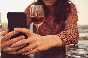 Beautiful elegant woman drinking wine and using cellphone outdoors.