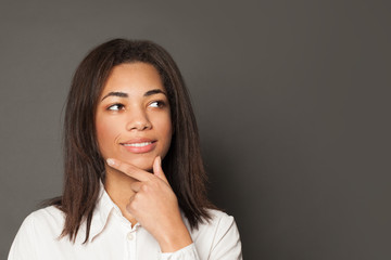Fototapeta premium Smart black girl student thinking and smiling on gray background