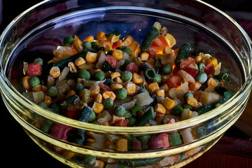 Frozen different vegetables in a glass plate on a wooden background.