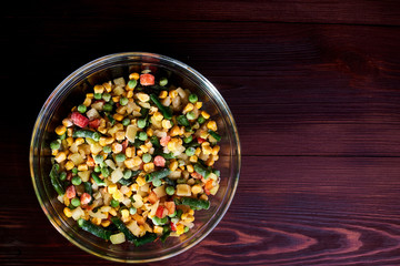 Frozen different vegetables in a glass plate on a wooden background.
