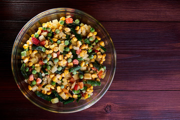 Frozen different vegetables in a glass plate on a wooden background.