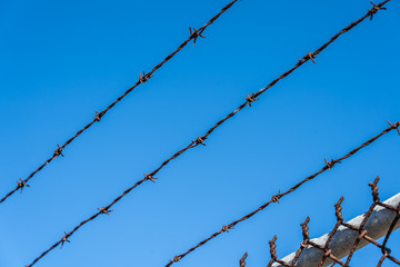 Metal fence with barbed wire on a blue sky