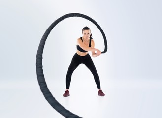 Woman doing exercises with battle rope. Photo of muscular model in sportswear isolated on white background