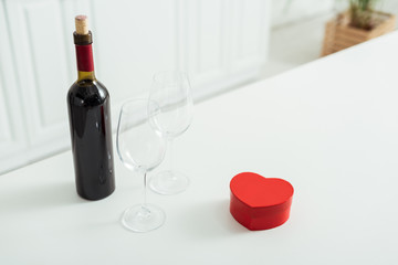 red heart-shaped gift box near empty glasses and bottle of wine
