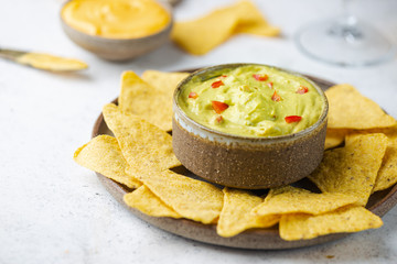 Nachos chips in a bowl with sauces guacamole and beer over white stone background.