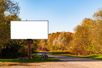 Blank white billboard for advertisement near the rural road. Sunny autumn day.