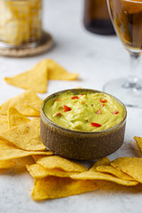 Nachos chips in a bowl with sauces guacamole and beer over white stone background.