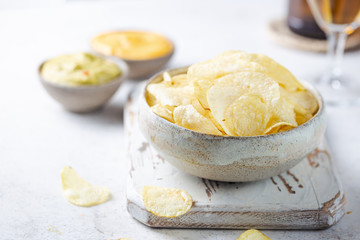 Crunchy delicious potato chips in a bowl with beer for a tasty snack break on light background