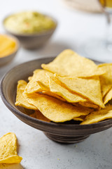 Nachos chips in a bowl with sauces and beer over white stone background.