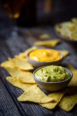 Nachos chips in a bowl with sauces guacamole and cheese, dip variety, over dark wooden background.