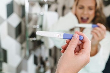 Image of young woman holding pregnancy test after shower in bathroom