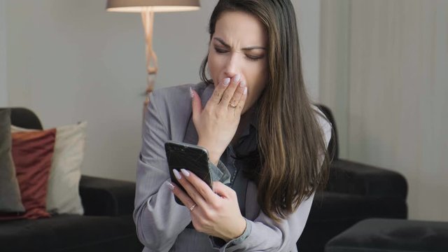 Footage of tired young business woman using mobile phone at her home after work.