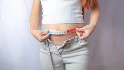 Pregnant woman is trying on her jeans or clothing that does not fit on her growing belly anymore in the first trimester