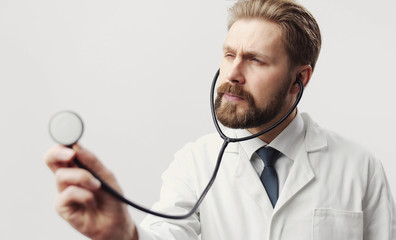 Close-up photo of concentrated male doctor using stethoscope isolated on white, healthcare concept