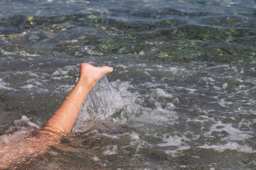 Closeup view horizontal photography of kids legs splashing in blue sea water outside swimming and enjoing summer beach vacations.