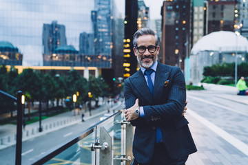 Smiling adult businessman with arms crossed on evening New York street