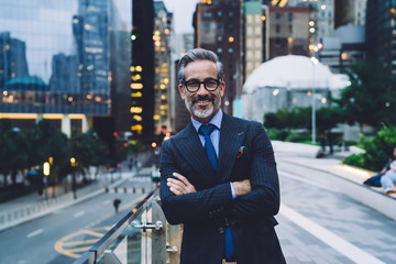 Smiling adult businessman with arms crossed against New York street