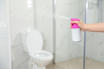 Woman spraying air freshener in bathroom, closeup