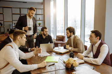 brainstorming time of business team in office, young men gathered together in office for discussing and sharing business ideas, planning strategy in modern boardroom, everyone in formal wear