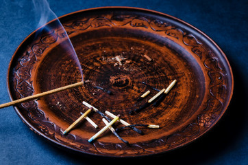 Indian aromatic sticks with smoke on a brown clay plate with matches on a dark table