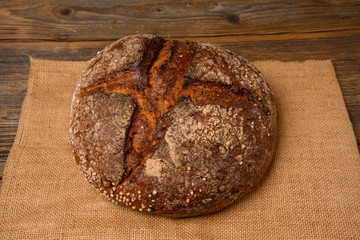 A fresh whole grain bread from the baker on a jute fabric on a rustic wooden background