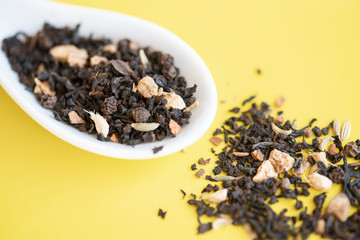 Dried tea leaves on the spoon. Yellow background.