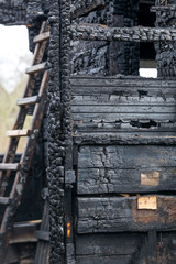 Charred boards of the interior walls of a room that burned in a fire with a staircase in the background.