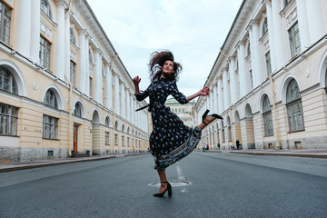 young woman in a brown dress jumps on the road on the street against the background of buildings in a classic style and smiles, the city of Saint Petersburg,