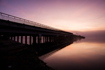 long diagonal bridge and river at dawn in the early morning in a haze of fog, nature and civilization