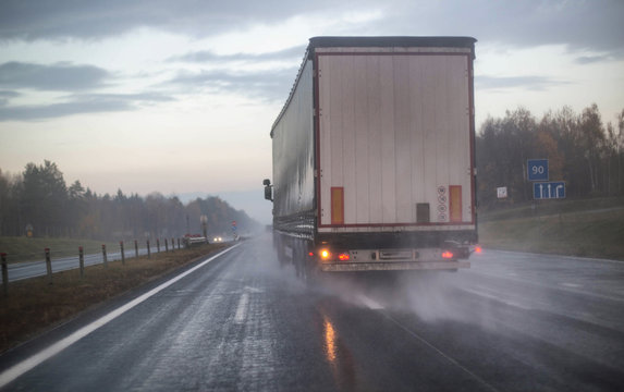 A truck with a trailer is being rebuilt on a motorway in a different row on slippery wet roads. The concept of security and attention to roads in bad weather, rain