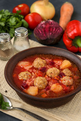 Soup with meatballs and vegetables in a dark bowl