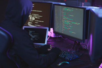 Back view of unrecognizable cyber security hacker wearing hood while working on programming code in...