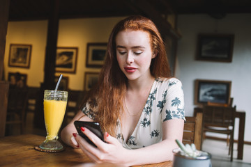 Relaxed woman using smartphone in cafe having drink