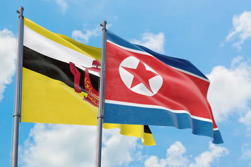 North Korea and Brunei flags waving in the wind against white cloudy blue sky together. Diplomacy concept, international relations.