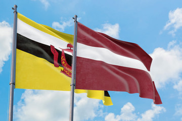 Latvia and Brunei flags waving in the wind against white cloudy blue sky together. Diplomacy concept, international relations.