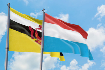 Luxembourg and Brunei flags waving in the wind against white cloudy blue sky together. Diplomacy concept, international relations.