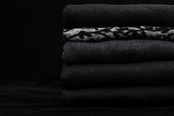 Black clothes and one gray with ornament in a pile on black background.