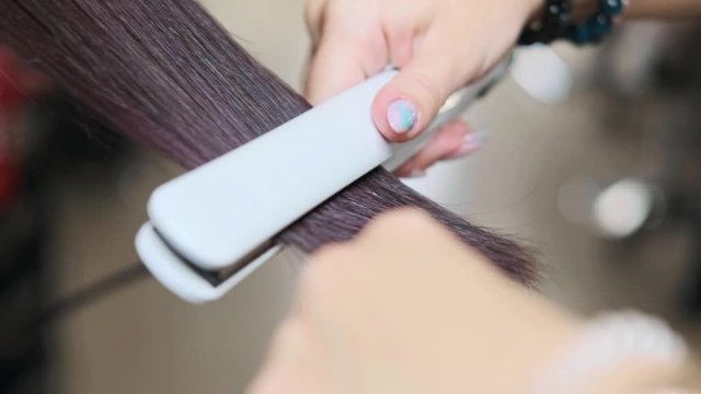The hairdresser straightens client's hair with irons in the salon. Close-up.