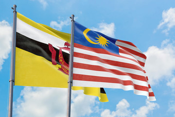 Malaysia and Brunei flags waving in the wind against white cloudy blue sky together. Diplomacy concept, international relations.