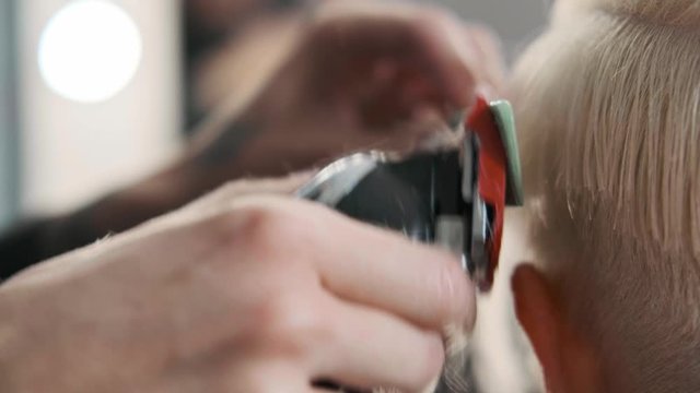 The hairdresser cuts blonde female client with a trimmer. A short pixie haircut and shaved temples . Ornament on the hair.