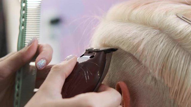 The hairdresser cuts blonde female client with a trimmer. A short pixie haircut and shaved temples . Ornament on the hair.