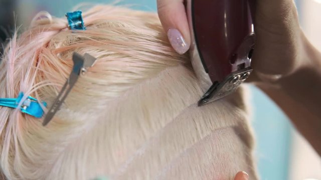 The hairdresser cuts blonde female client with a trimmer. A short pixie haircut and shaved temples . Ornament on the hair.
