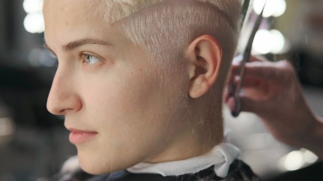 The hairdresser cuts dyed hair female client with scissors. A short pixie haircut and shaved temples . Ornament on the hair.