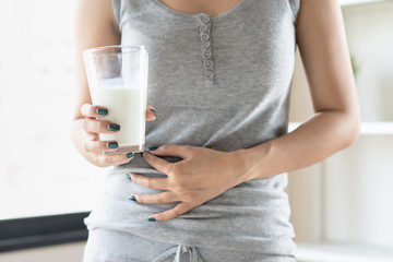 lactose intolerance concept. Woman holding a glass of milk and having a stomachache. - obrazy, fototapety, plakaty